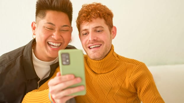 Happy gay couple sitting on the sofa using a mobile phone