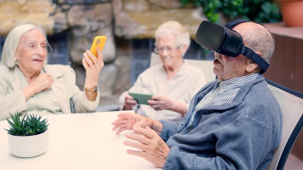 Senior woman taking photos with mobile phone in a geriatric while a mate using VR goggles