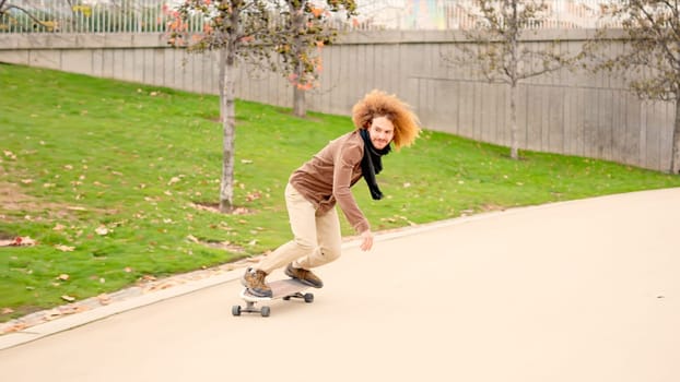 An alternative young man with curly hair skateboarding in a n urban park