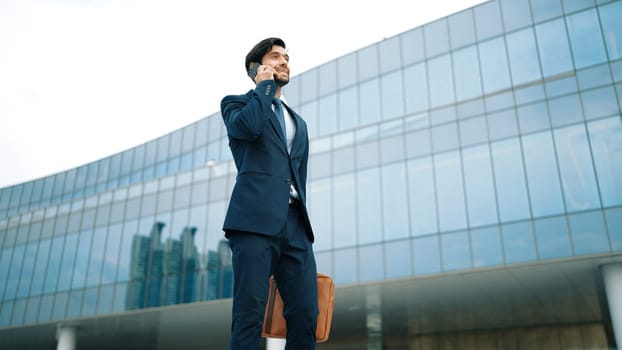 Smart business man using phone to talking while walking at building. Happy manager walking at street while talking on smart phone to discuss business plan or marketing strategy or working. Exultant.