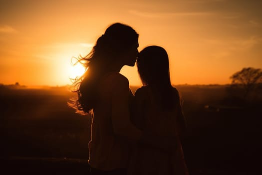 Silhouette of mother and daughter hugging each other in the sunset light.