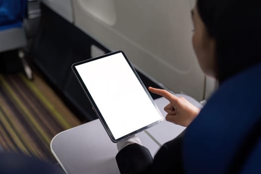 Woman traveler or passenger sits at the window seat, using his portable digital tablet touchpad during the flight. tablet white screen mockup.