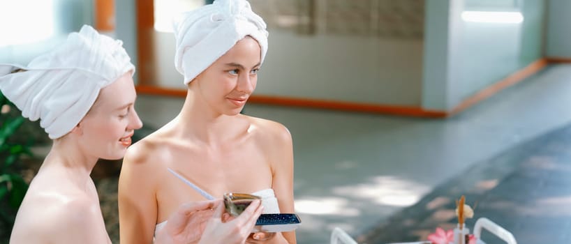 A portrait of two beautiful caucasian woman in white towel using homemade facial mask rounded by peaceful natural environment at outdoor. Healthy and beauty concept. Blurring background. Tranquility.