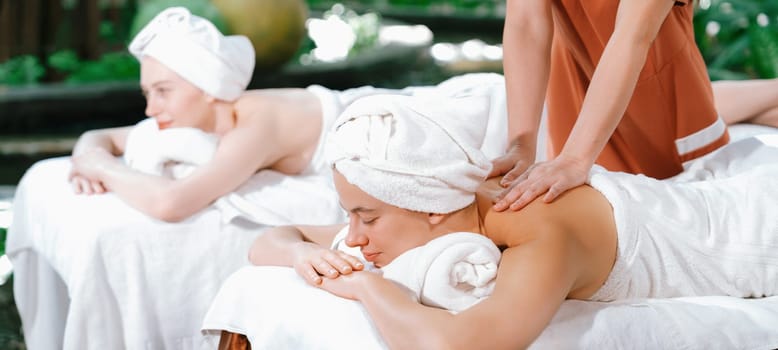 A portrait of two young attractive woman lie on bed during having back massage by a professional masseur at outdoor surrounded by peaceful natural environment. Healthy and beauty concept. Tranquility.