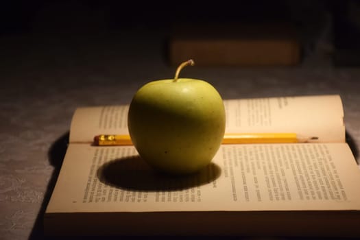 A stack of books in red covers and a red apple against the morning window. A metaphorical image of a good start to the day and life.