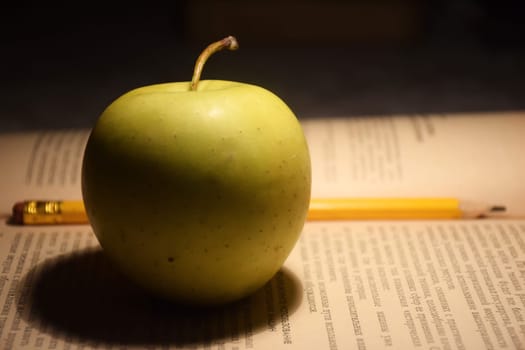 A stack of books in red covers and a red apple against the morning window. A metaphorical image of a good start to the day and life.