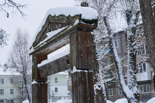Photo an old wooden gate post on the background of residential buildings. Winter and snow.