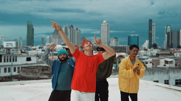 Multicultural teenagers dancing while looking at camera on rooftop with urban city view. Professional break dance group moving to hip-hop music with friends cheer. Outdoor sport 2024. Endeavor.
