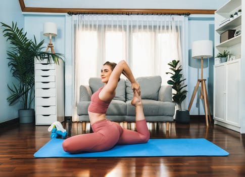 Flexible and dexterity woman in sportswear doing yoga position in meditation posture on exercising mat at home. Healthy gaiety home yoga lifestyle with peaceful mind and serenity.