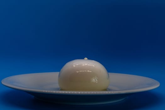 A burrata cheese rests delicately on a white plate against a vivid blue background.