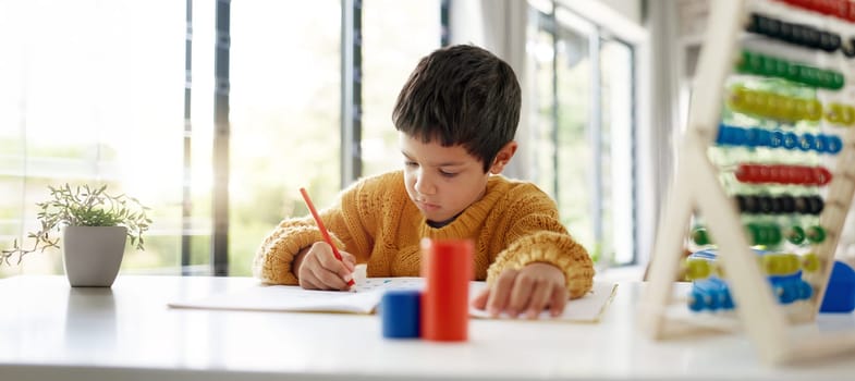 Student, drawing or child writing homework on notebook in kindergarten education for growth development. Project, creative boy or kid artist with color pencil learning or working on sketching skills.