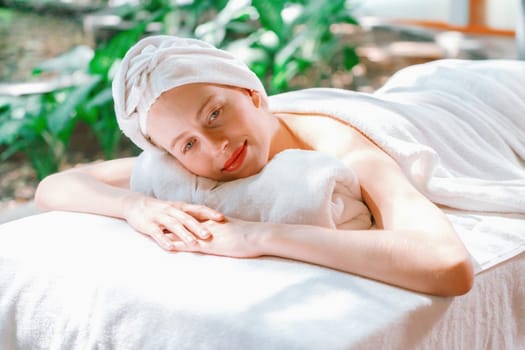 Beautiful young woman relaxes on a spa bed surrounded by nature. ready for a body massage. Attractive female in white towel lying peacefully during waiting for body massage. Close up. Tranquility