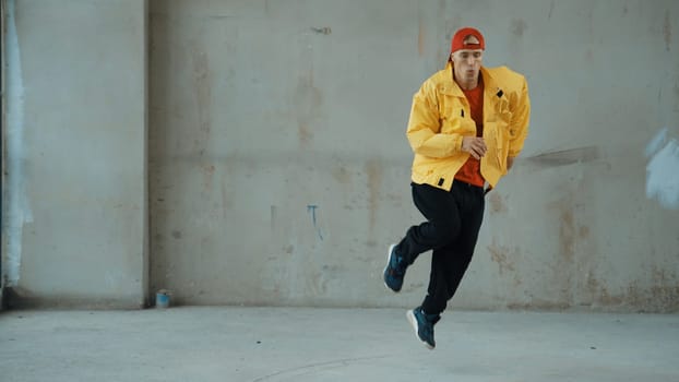 Caucasian hipster shows or practicing footstep at street, urban city. Motion shot of young stylish break dancer moving and stretch arm and leg. Outdoor sport 2024. Gray background. Endeavor.