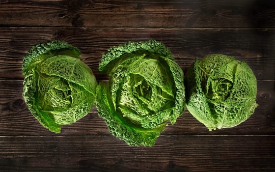 Three savoy cale cabbage heads on dark wooden board, view from above