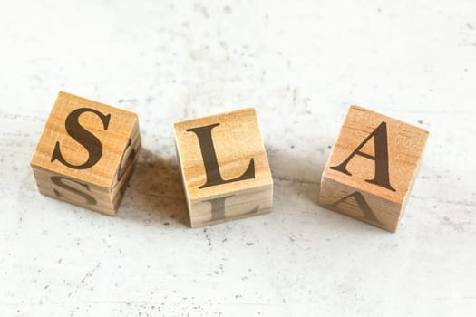 Three wooden cubes with letters SLA (stands for Service Level Agreement) on white board.