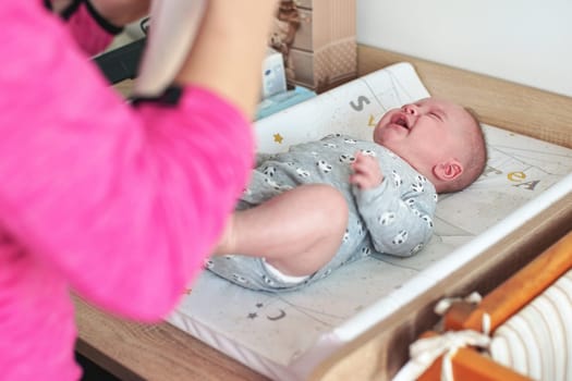 4 months old baby infant boy on changing board, crying as mother is putting his clothes on