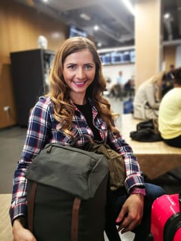 Young woman in shirt waiting for her transfer, with her backpack and luggage near her, blurred station in background