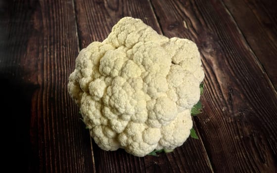 Closeup on whole white raw cauliflower vegetable on dark wooden board