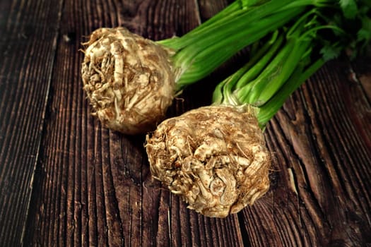 Celery root with green leaves on dark wooden board