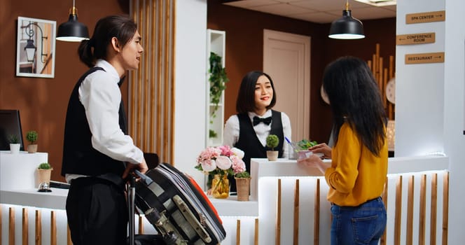 Front desk staff giving key card and passport after check in, asian woman arriving at five star hotel and registering. Traveler receiving room access and id documents, ensuring pleasant stay.