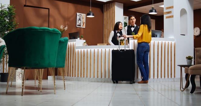 Asian woman approaching front desk in hotel lobby, receptionist asking client about room reservation details for check in. Friendly employee welcoming customer at reception, hospitality industry.