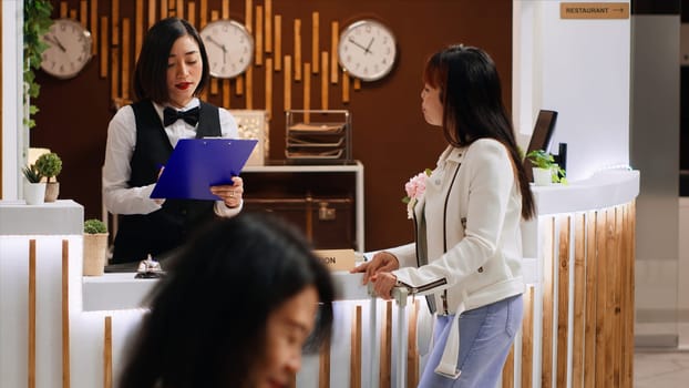 Hotel guest signing registration papers at front desk, confirming room reservation and enjoying five star resort facilities. Asian woman finishing with check in process, concierge services.