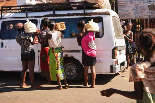 Toliara, Madagascar - May 05, 2019: Group of unknown Malagasy women selling food to passengers in white bus. There are not many shops, goods are usually sold by the road in this region.