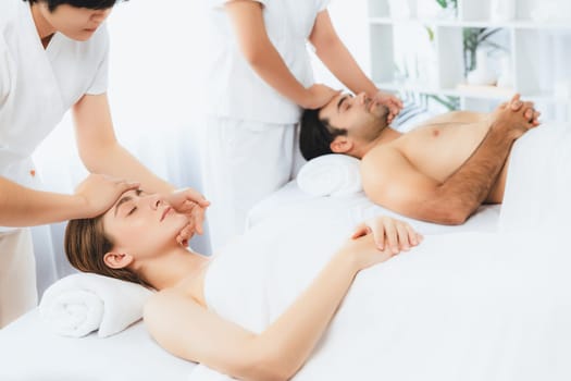 Caucasian couple enjoying relaxing anti-stress head massage and pampering facial beauty skin recreation leisure in dayspa modern light ambient at luxury resort or hotel spa salon. Quiescent