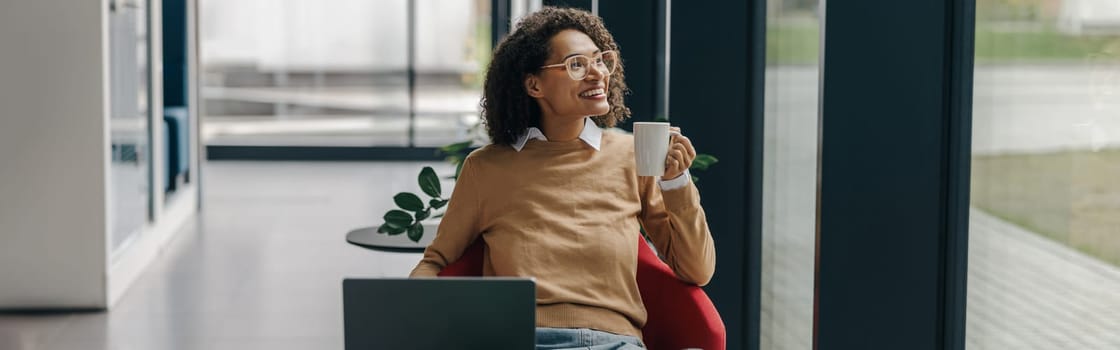 Smiling female freelancer have coffee break during working on laptop in modern coworking