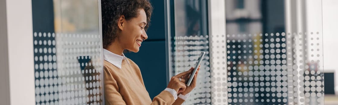 Stylish business woman is using phone standing in office during break time. High quality photo