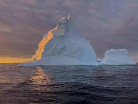 A huge high breakaway glacier drifts in the southern ocean off the coast of Antarctica at sunset, the Antarctic Peninsula, the Southern Arctic Circle, azure water, cloudy weather. High quality photo