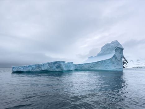 A huge high breakaway glacier drifts in the southern ocean off the coast of Antarctica at sunset, the Antarctic Peninsula, the Southern Arctic Circle, azure water, cloudy weather. High quality photo