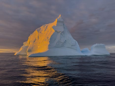 A huge high breakaway glacier drifts in the southern ocean off the coast of Antarctica at sunset, the Antarctic Peninsula, the Southern Arctic Circle, azure water, cloudy weather. High quality photo