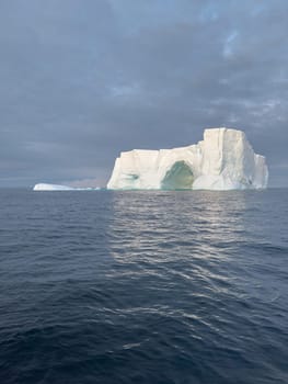 A huge high breakaway glacier drifts in the southern ocean off the coast of Antarctica at sunset, the Antarctic Peninsula, the Southern Arctic Circle, azure water, cloudy weather. High quality photo