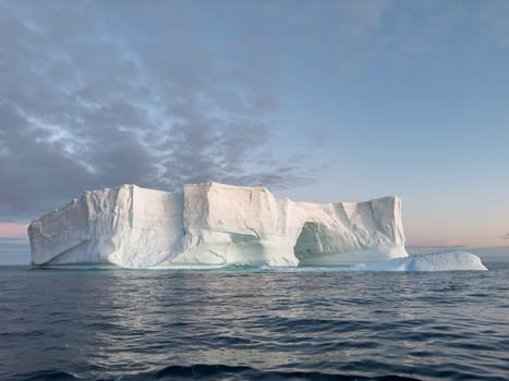 A huge high breakaway glacier drifts in the southern ocean off the coast of Antarctica at sunset, the Antarctic Peninsula, the Southern Arctic Circle, azure water, cloudy weather. High quality photo