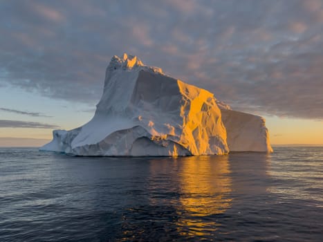 A huge high breakaway glacier drifts in the southern ocean off the coast of Antarctica at sunset, the Antarctic Peninsula, the Southern Arctic Circle, azure water, cloudy weather. High quality photo