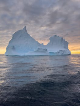 A huge high breakaway glacier drifts in the southern ocean off the coast of Antarctica at sunset, the Antarctic Peninsula, the Southern Arctic Circle, azure water, cloudy weather. High quality photo