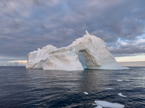 A huge high breakaway glacier drifts in the southern ocean off the coast of Antarctica at sunset, the Antarctic Peninsula, the Southern Arctic Circle, azure water, cloudy weather. High quality photo