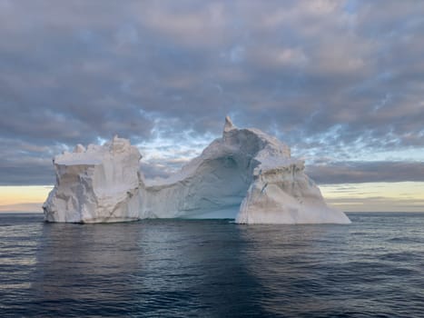 A huge high breakaway glacier drifts in the southern ocean off the coast of Antarctica at sunset, the Antarctic Peninsula, the Southern Arctic Circle, azure water, cloudy weather. High quality photo