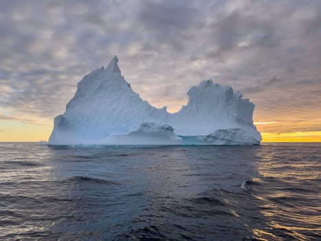 A huge high breakaway glacier drifts in the southern ocean off the coast of Antarctica at sunset, the Antarctic Peninsula, the Southern Arctic Circle, azure water, cloudy weather. High quality photo