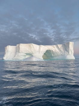 A huge high breakaway glacier drifts in the southern ocean off the coast of Antarctica at sunset, the Antarctic Peninsula, the Southern Arctic Circle, azure water, cloudy weather. High quality photo