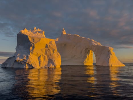 A huge high breakaway glacier drifts in the southern ocean off the coast of Antarctica at sunset, the Antarctic Peninsula, the Southern Arctic Circle, azure water, cloudy weather. High quality photo