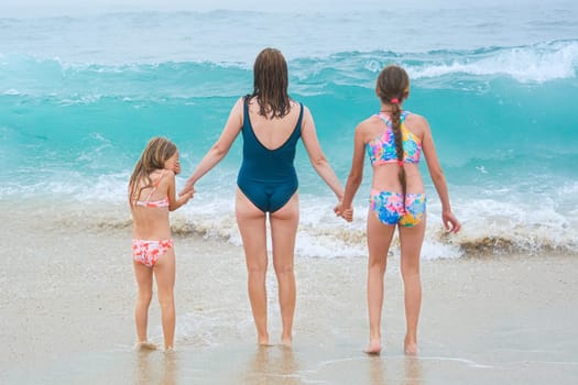 Mother and children playing on the ocean beach. Family enjoying the ocean. Mother holds girls's hands and they all look at the ocean together.