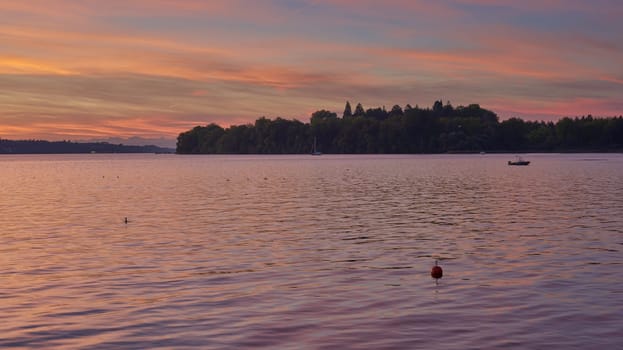 Bodensee Lake Sunrise Panorama. Morning Sunlight Over Tranquil Waters. Witness the mesmerizing dawn over Germany's Bodensee Lake, captured from a boat dock. Embrace the tranquil beauty of the early morning as the sun rises, casting a soft glow on the landscape. The peaceful scene features boats, yachts, and a charming water shack set against a backdrop of a captivating sky. Clouds delicately reflect on the calm water, creating a serene atmosphere. Immerse yourself in the serene beauty of a lakeside sunrise. Explore the harmony of nature, technology, and production as the day unfolds by the lake.