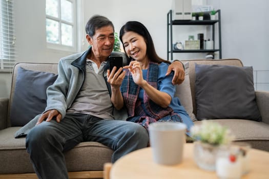 Retired elderly couple sits on couch using mobile together and relax in their home. Senior Activity Concept.