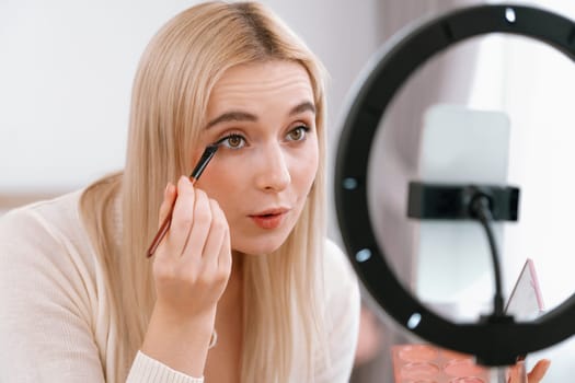 Young woman making beauty and cosmetic tutorial video content for social media. Beauty blogger using camera and light ring while showing how to apply eyeshadow to audience or follower. Blithe
