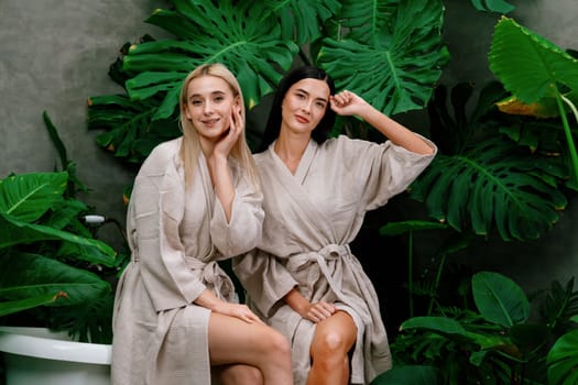 Tropical and exotic spa garden with bathtub in modern hotel or resort with young two women in bathrobe enjoying leisure and wellness lifestyle surrounded by lush greenery foliage background. Blithe