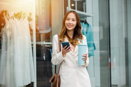 Coffee break in the city ,young woman holding a tumbler mug and smartphone in front of an office building. Hot beverage and digital communication is her convenience.