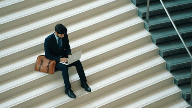 Top view of investor working or planing strategy by using laptop at stair. Professional business man wearing suit while working and typing data analysis by using laptop at modern hotel. Exultant.