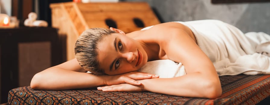 Beautiful relaxing caucasian woman lie on spa bed in front of wooden sauna cabinet. Young and healthy woman waiting for massage treatment in warm traditional spa room. Tranquility.